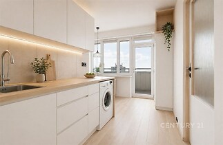 Světlá moderní kuchyň s dřevěnou pracovní deskou, bílými skříňkami a parketovou podlahou, velká okna s balkonovými dveřmi poskytují dostatek světla.