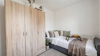 Útulná ložnice s dřevěnou vestavěnou skříní, moderní dekor a světlé stěny vytvářejí příjemnou atmosféru.