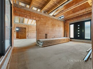 Nezařízený obývací pokoj s betonovou podlahou, dřevěným stropem a velkými okny, připravený k rekonstrukci v moderním stylu