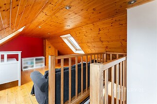 Podkrovní pokoj s dřevěným obložením, parketovou podlahou a střešními okny, vytvářející světlý a útulný prostor.