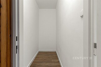 Úzká chodba s laminátovou podlahou a bílými stěnami, moderní interiér, vhodná pro vestavěné skříně nebo úložné prostory.