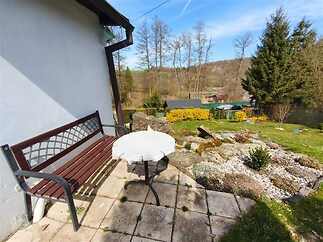 Zahrada s dlážděnou terasou a lavičkou, obklopená zelení a vzrostlými stromy, ideální pro relaxaci v klidném prostředí.