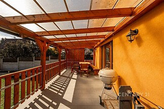 Prostorná zastřešená terasa s dřevěnou konstrukcí a dlažbou, ideální pro venkovní posezení, nabízí soukromí a přímý vstup na zahradu.