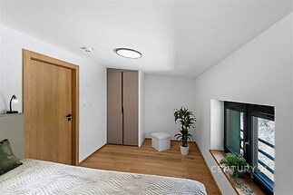 Ložnice s parketovou podlahou, vestavěnou skříní a moderními černými okny, která poskytují světlý a vzdušný prostor.