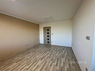 Prázdná místnost s parketovou podlahou a dřevěnými dveřmi, světlé stěny nabízejí moderní prostor připravený k užívání.