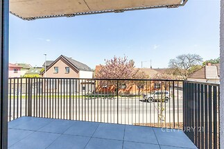 Balkon s moderní dlažbou a kovovým zábradlím, poskytující výhled na klidnou ulici a okolní rodinné domy, ideální pro relaxaci.