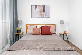 Prostorná ložnice s parketovou podlahou, velkými okny a moderním nábytkem, vytváří světlý a útulný prostor pro relaxaci.