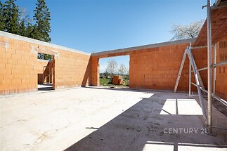 Rozestavěný pokoj s odkrytou cihlou a betonovou podlahou, prostorná dispozice s velkými okny, moderní výstavba na klidném místě.