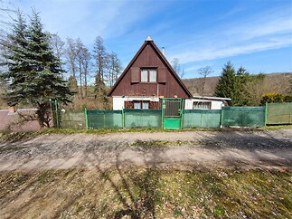 Chata na okraji lesa s dřevěným vzhledem, zelený plot a zahrada. Skvělá rekreační nemovitost v klidném prostředí.