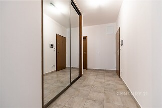 Předsíň s dlažbou a vestavěnými skříněmi, moderní interiér se světlými zdmi a dřevěnými dveřmi, poskytuje prostorný vstupní prostor.