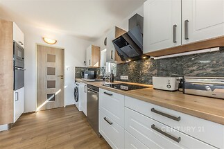 Moderní kuchyň s parketovou podlahou, vestavěnými spotřebiči a dřevěnými pracovními deskami, světlý interiér s elegantními skříňkami.