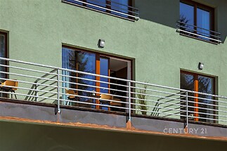 Balkon s moderním zábradlím, francouzskými okny a zelenou fasádou, nabízí příjemný výhled, ideální pro relaxaci a venkovní posezení.