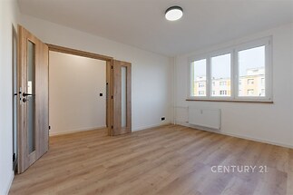 Světlý obývací pokoj s parketovou podlahou, dřevěnými dveřmi a velkými okny, moderní interiér v rekonstruovaném bytě.