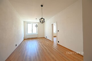 Světlý obývací pokoj s parketovou podlahou, moderní závěsné osvětlení a velká okna pro přirozené světlo, v rekonstruovaném stavu