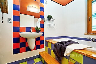 Barevná koupelna s moderními obklady, dřevěnými schody a velkým umyvadlem, světlý design doplněný dekorativními prvky a velkým oknem