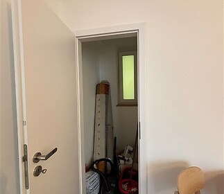 Malá úložná komora s parketovou podlahou a bílými stěnami, kombinace moderního stylu a praktického prostoru pro skladování, bez oken.