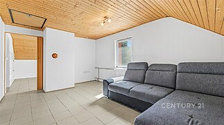 Světlý obývací pokoj s dlažbou a dřevěným stropem, velká okna zajišťují dostatek přirozeného světla, moderní a útulný interiér.