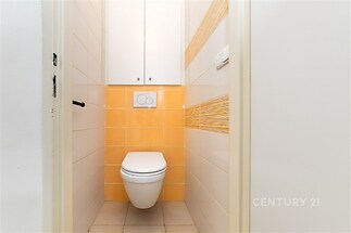 Malá moderní toaleta s oranžovým obkladem, bílými stěnami a vestavěnou skříní nabízí efektivní využití prostoru.