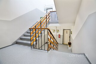 Světlé schodiště s moderní dlažbou a dřevěným zábradlím, které vytváří čistý a udržovaný prostor v obytném domě.