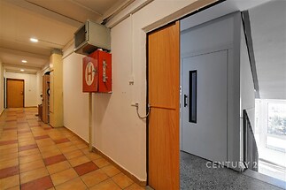 Společná chodba v bytovém domě s dlažbou na podlaze, dřevěnými dveřmi a přístupem k výtahu, zachovalá a dobře udržovaná.