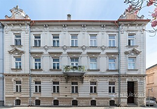 Historická budova s dekorativní fasádou a balkonem, zdobené detaily a udržovaný vchod, ideální pro městské bydlení.