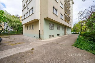 Exteriér bytového domu s udržovaným chodníkem a prostornou zelení, ideální pro městské bydlení, světlá fasáda, dobře dostupná lokalita