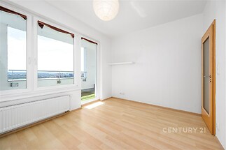 Světlý obývací pokoj s parketovou podlahou, velká okna poskytují výhled na terasu, moderní bílá stěna, útulný a prostorný interiér