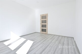 Světlý prázdný pokoj s laminátovou podlahou, dřevěnými dveřmi a bílými stěnami, ideální pro moderní interiérové úpravy.