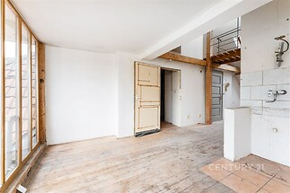 Světlý obývací pokoj s dřevěnou podlahou, velkými okny a otevřeným dispozicem. Prostor je ideální pro moderní úpravu a má potenciál pro rekonstrukci.