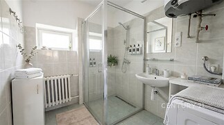 Světlá koupelna s moderní dlažbou a sprchovým koutem, nabízí funkční vytápění a úložné prostory, optimalizovaná pro komfortní bydlení.