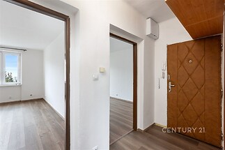 Chodba s moderními dřevěnými podlahami, světlými stěnami a vestavěným osvětlením, vedoucí do pokojů s velkými okny.