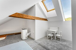 Podkrovní pokoj s kobercem, dřevěné trámy a střešní okno. Moderní styl, ideální pro dětský koutek nebo pracovní prostor.