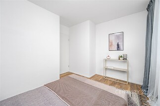 Prostorná ložnice s parketovou podlahou, moderní dekorace a velká okna, která poskytují dostatek přirozeného světla.