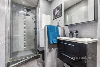 Moderní koupelna s šedou dlažbou, sprchovým koutem a černým umyvadlovým stolkem. Elegantní design a kvalitní povrchy.