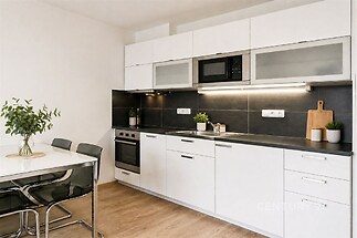 Moderní kuchyň s parketovou podlahou, bílá kuchyňská linka, vestavěné spotřebiče, světlý jídelní kout, elegantní design.