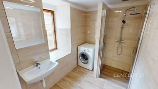 Koupelna s přírodní dlažbou, sprchovým koutem a velkým oknem, nabízí moderní design a dostatek denního světla.