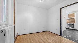 Světlá kuchyň s parketovou podlahou, moderní spotřebiče, přechod do obývacího pokoje s dlažbou, bílá výmalba.