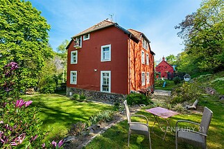 Červená historická vila s kamennými prvky, obklopená upravenou zahradou, nabízí velká okna a tradiční styl v klidné lokalitě.