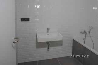 Moderní koupelna s bílou dlažbou, šedými obklady a vanou, vybavená umyvadlem a chromovými doplňky