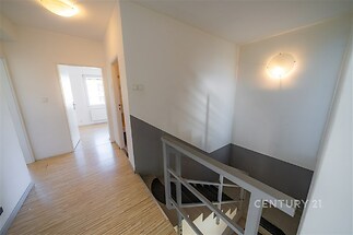 Chodba s dřevěnou podlahou, moderní osvětlení, schodiště s kovovým zábradlím, světlý interiér, přístup do dalších místností.