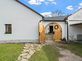 Venkovní dvůr s dřevěnými vraty, kamennou cestou a udržovaným trávníkem nabízí rustikální kouzlo a atmosféru klidného venkova.