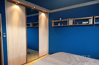 Ložnice s parketovou podlahou, vestavěné skříně s posuvnými dveřmi a tmavě modré stěny vytvářejí moderní a elegantní prostor.