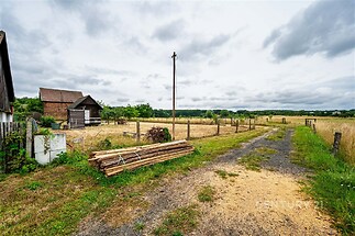 Prázdný venkovský pozemek s velkým otevřeným prostranstvím, sousedstvím s přírodou a okolními pastvinami, ideální pro stavbu nebo zemědělství.