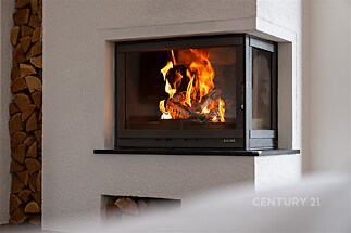 Krbová kamna s moderním designem, bílé omítkové zdi a připravené dřevo na topení.