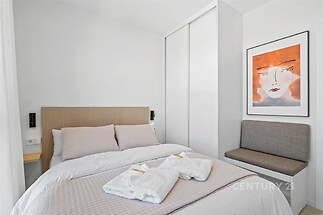 Světlá ložnice s vestavěnými skříněmi, moderní dekorací na stěně a pohodlným lůžkem, ideální pro klidný odpočinek