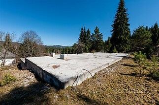 Základová deska na rozlehlém pozemku, připravená k nové výstavbě, obklopená přírodou a vzrostlými stromy, ideální pro klidné bydlení