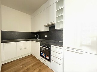 Moderní kuchyň s lesklými bílými skříňkami, vestavěnými spotřebiči a dřevěnou podlahou, nabízí elegantní prostor pro vaření.