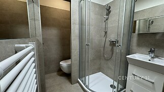 Moderní koupelna s rohovým sprchovým koutem, světle šedé dlažby a závěsným WC, vestavěné skříně nabízí elegantní řešení úložného prostoru.