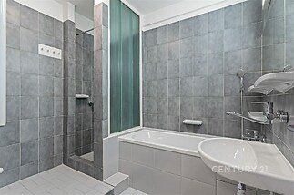 Prostorná koupelna s šedou dlažbou, sprchovým koutem, vanou a moderními armaturami, zajišťující komfort a elegantní vzhled.