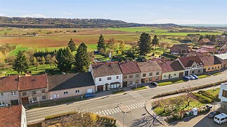 Pohled na řadové domy v klidné ulici s výhledem na okolní krajinu, každý dům má sedlovou střechu a menší zahrádku, ideální pro rodinné bydlení